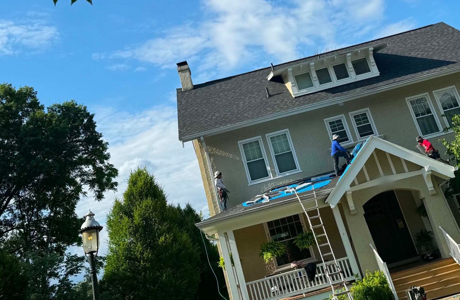 Crew laying ice-and-water shield across a front porch roof on an older stucco home